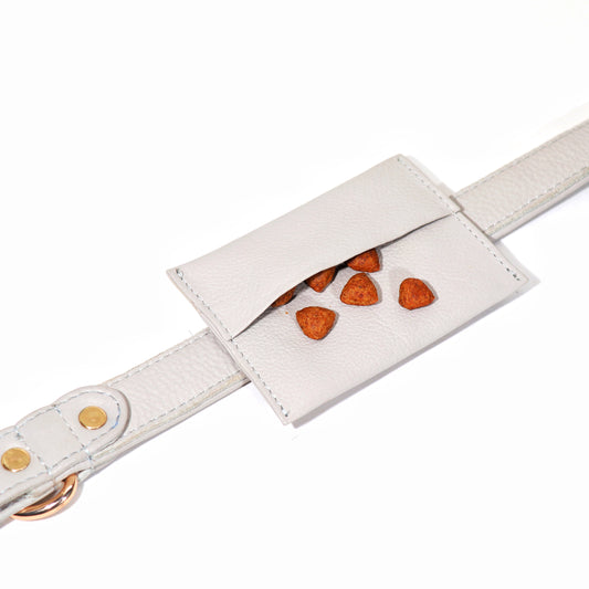 A beige dog treat pouch with a white strap and a pocket featuring a paw print design, with metal hardware accents.