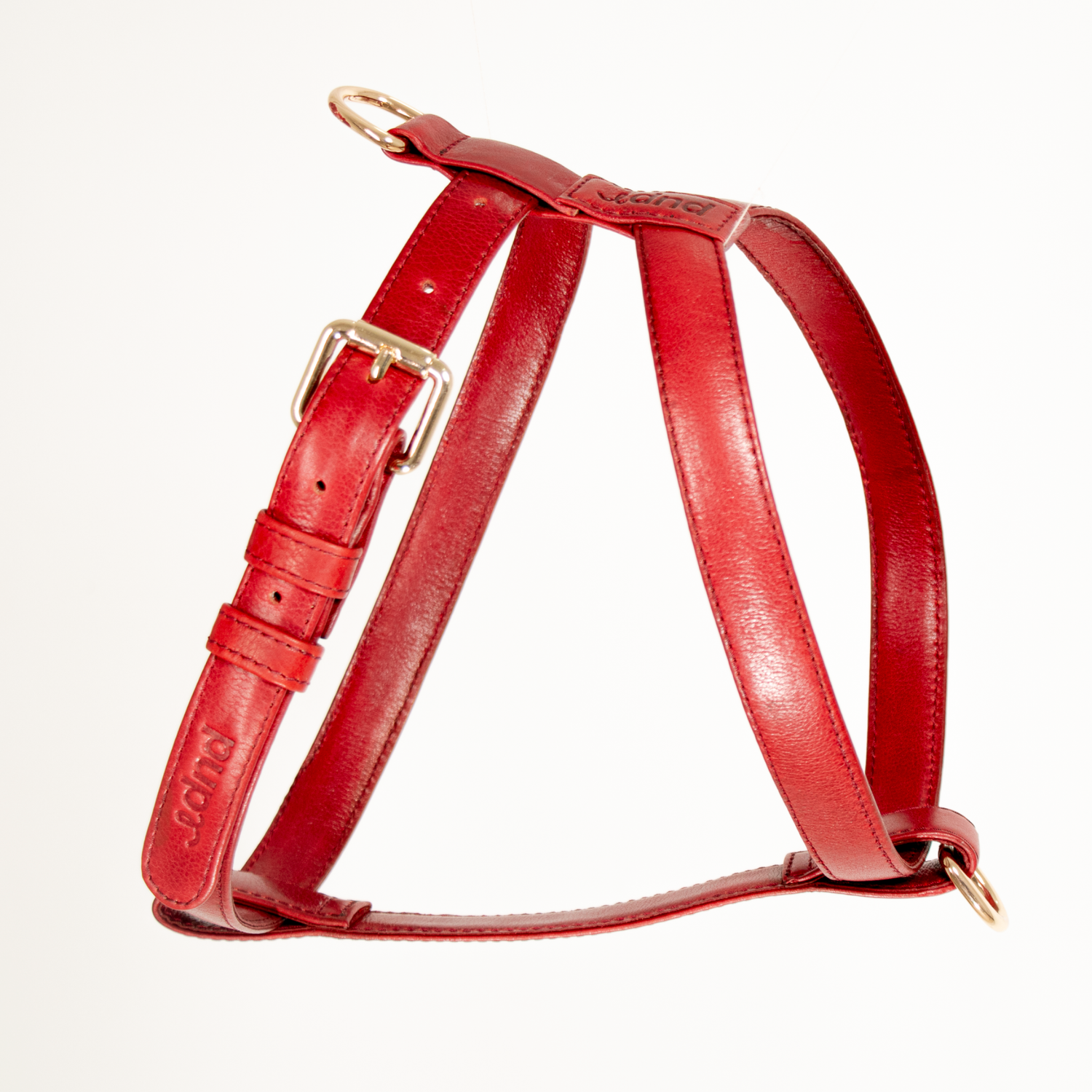 Red leather dog harness with gold hardware on a white background